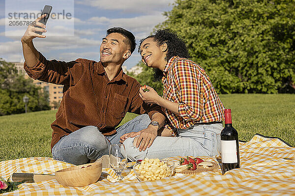 Smiling boyfriend taking selfie with girlfriend through smart phone at park