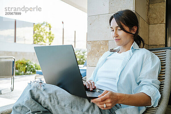 Businesswoman using laptop sitting on lounge chair at back yard