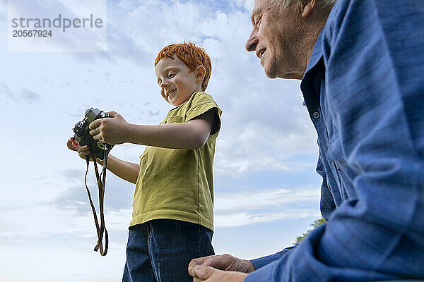 Smiling boy looking at old camera by grandfather