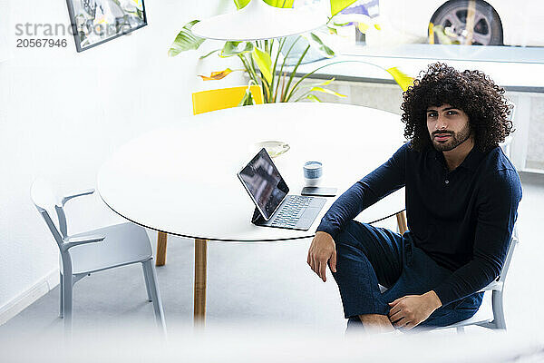 Confident young businessman with tablet PC sitting at table in office