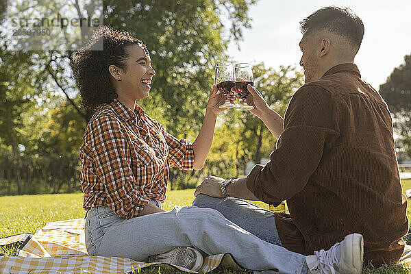 Cheerful young couple celebrating with wine and sitting at park