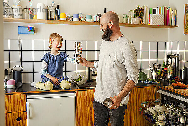 Smiling father playing with daughter sitting on kitchen counter at home