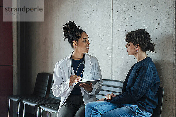 Doctor with tablet PC discussing with patient on chair in hospital