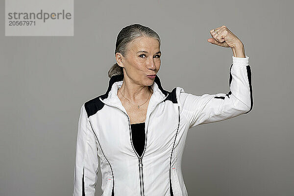 Senior woman puckering and flexing muscle against gray background