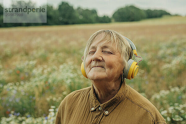 Smiling senior woman listening to music through wireless headphones at chamomile field