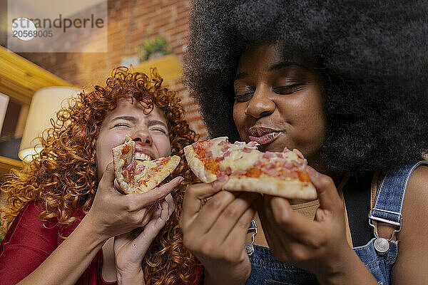 Multiracial friends eating slice of pizza at home