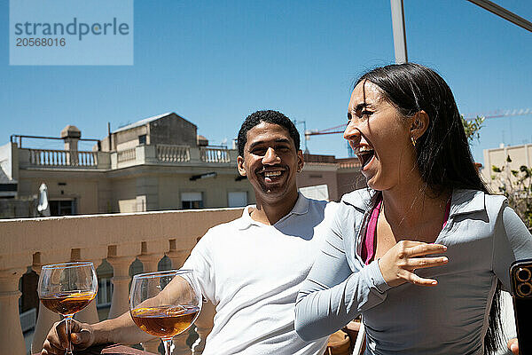 Cheerful young couple sitting with drinks at terrace on sunny day