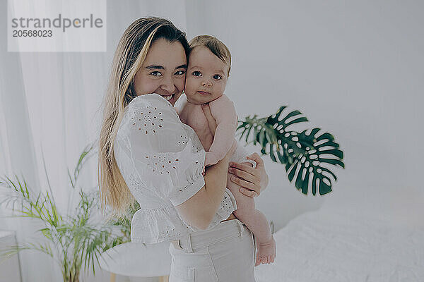 Cheerful woman holding baby boy and standing at home