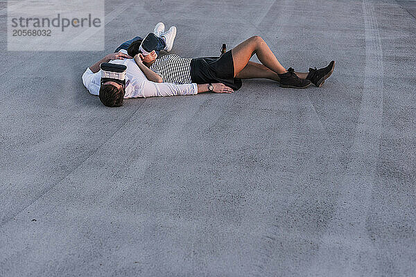 Young couple with virtual reality headset lying down on asphalt