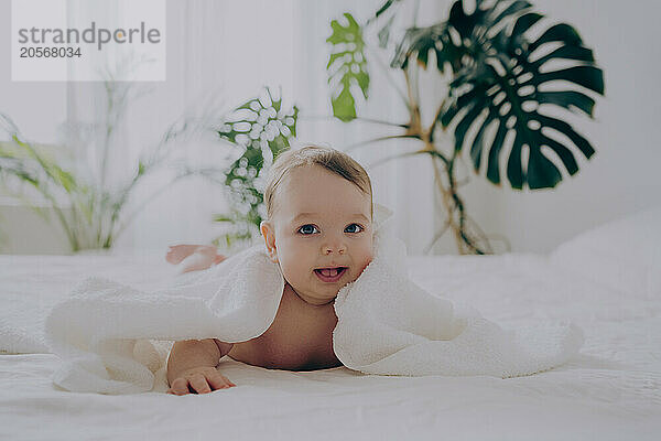 Cute boy playing with towel and lying on bed at home