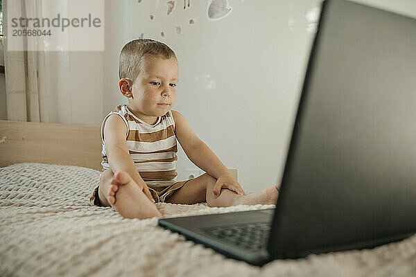 Boy watching cartoon on laptop sitting in bedroom at home