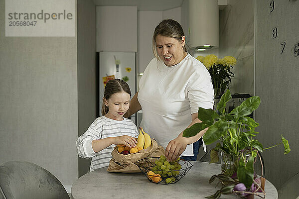 Mother and daughter keeping fruits in basket on table at home