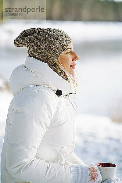 Smiling woman wearing knit hat holding cup of tea