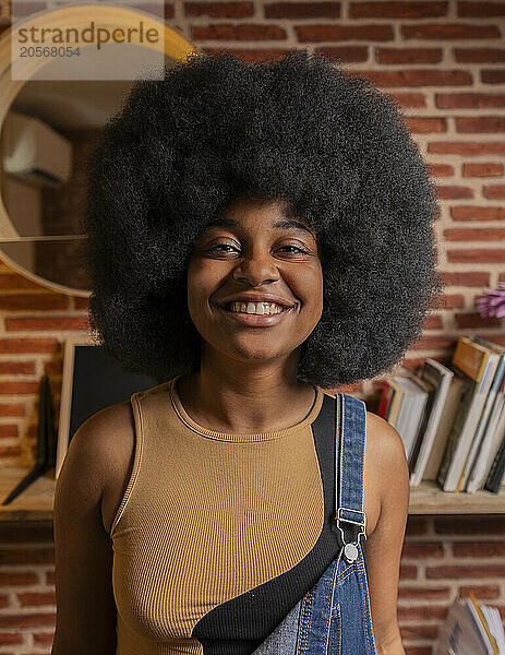 Happy Afro woman in bib overalls at home