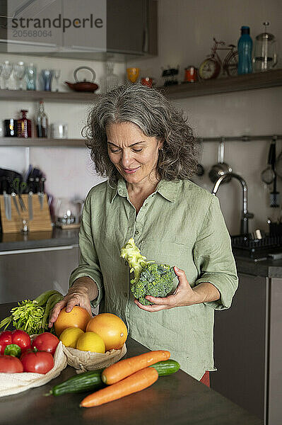 Gray hair woman holding taking out groceries and standing in kitchen