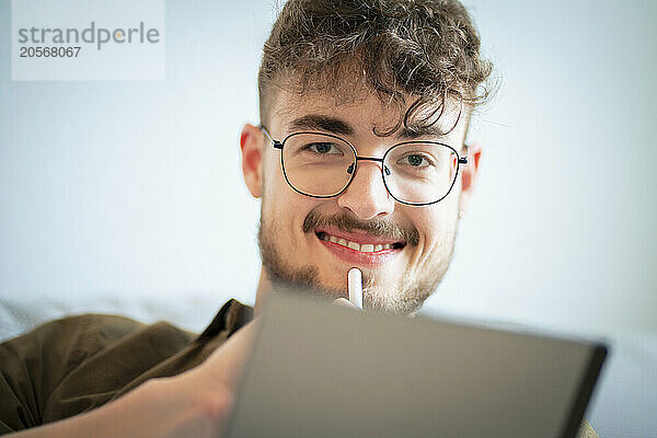 Smiling handsome young man wearing eyeglasses using tablet PC at home