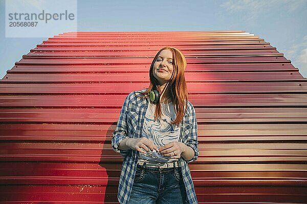 Young teenage girl with wireless headphones and standing in front of red structure