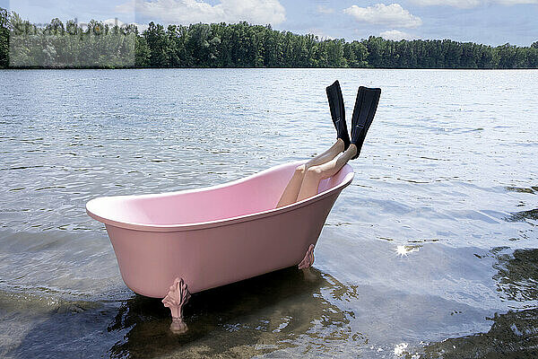 Legs of girl wearing diving flipper inside pink bathtub in lake