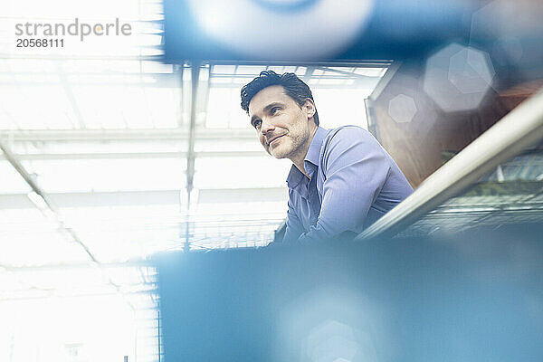 Smiling mature businessman leaning on railing at airport terminal