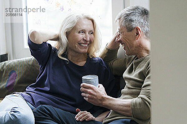 Happy retired senior couple sitting with coffee cup at home