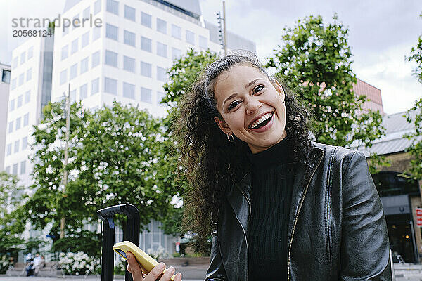 Cheerful young beautiful woman using mobile phone in city