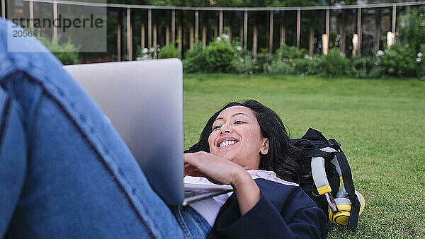 Smiling businesswoman working on laptop lying down at office park