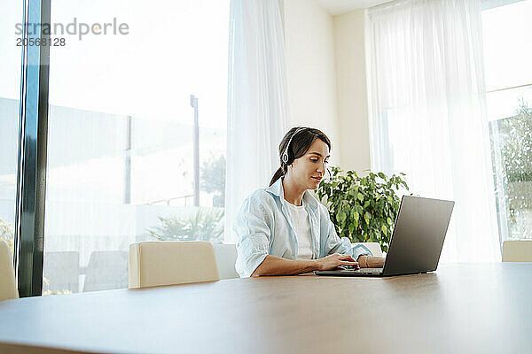 Confident customer service representative with headset using laptop at table working from home