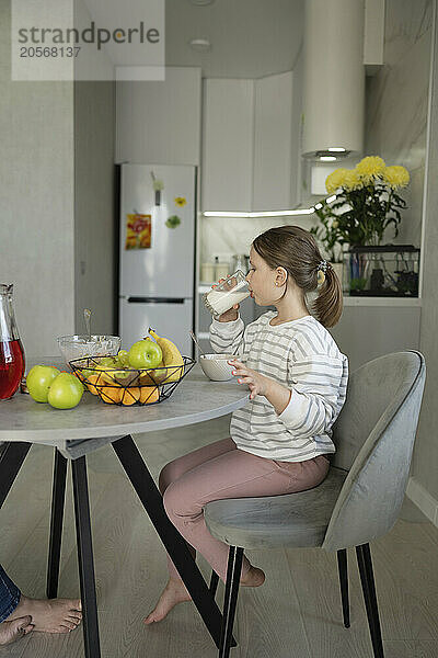 Girl drinking milk sitting on chair at home