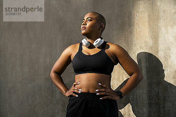 Confident sporty woman standing with arms akimbo in front of wall