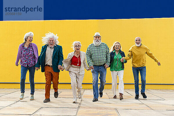 Group of senior happy friends holding hands and running on footpath