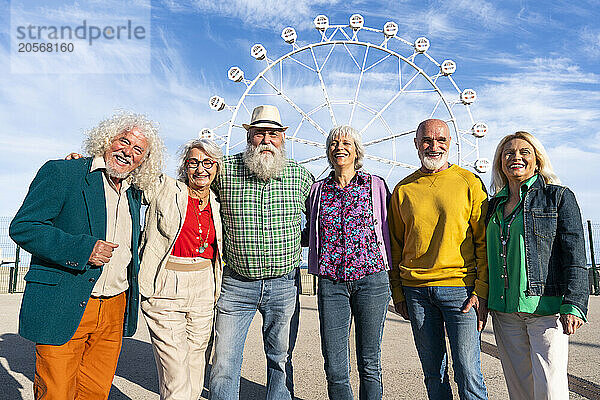 Retired men and women standing side by side in front of Ferris wheel on sunny day