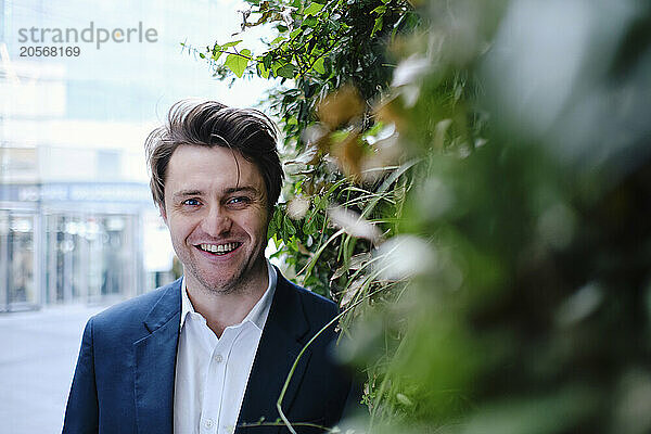 Happy businessman standing near plants