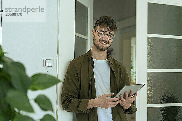 Smiling young man with tablet PC standing at doorway