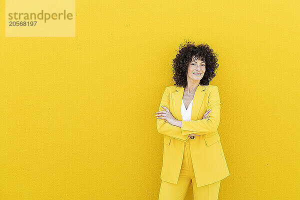 Smiling beautiful woman with arms crossed standing in front of yellow wall