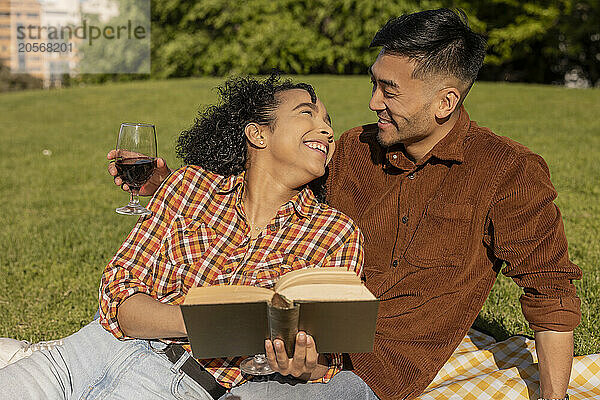 Happy woman holding book and leaning on boyfriend at park