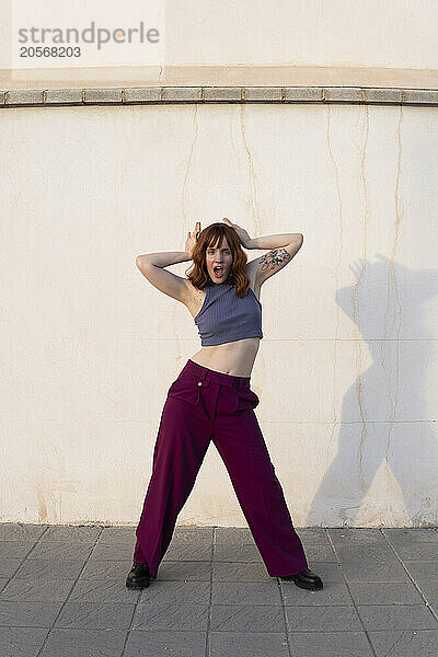 Confident woman with arms outstretched dancing on footpath in front of white wall