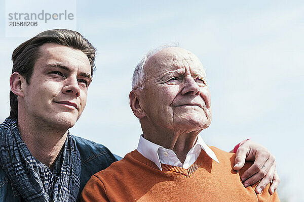 Smiling young man with grandfather under sky