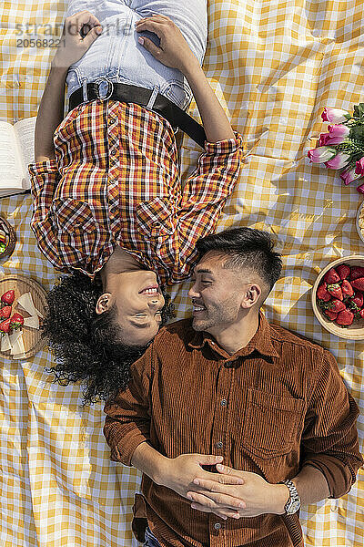 Happy multiracial couple lying face to face on picnic blanket