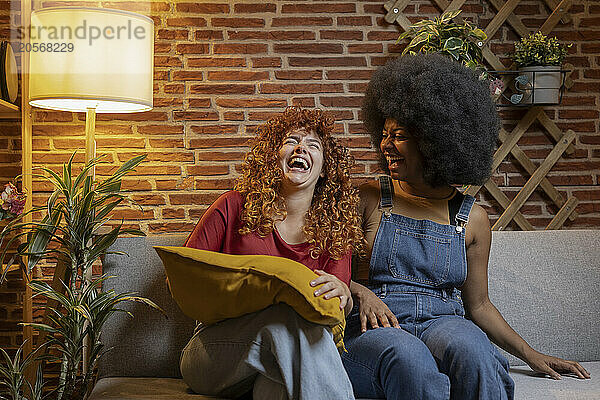 Cheerful multiracial young friends enjoying leisure time sitting on sofa at home