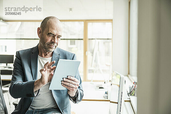 Confident mature businessman using tablet PC sitting at workplace