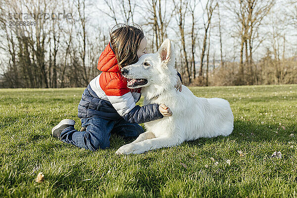 Boy embracing White Swiss Shepherd Dog on grass in meadow