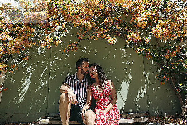 Affectionate couple sitting in shade under bougainvillea vine