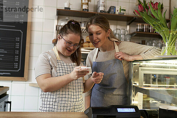 Smiling cafe owner with down syndrome learning cash register in coffee shop