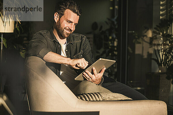 Happy man using tablet PC on sofa at home