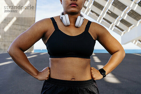 Sporty woman with arms akimbo standing on road