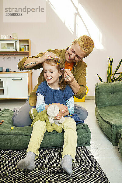 Mother clipping daughter's hair sitting on couch at home