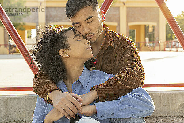 Young man with arm around girlfriend sitting at park