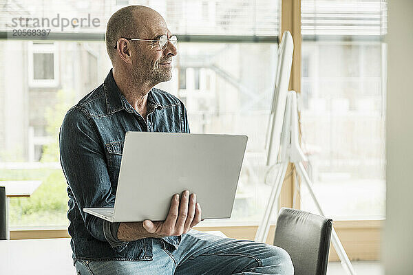 Mature businessman sitting with laptop in office