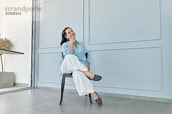 Smiling businesswoman sitting on chair near blue wall at office