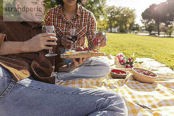 Young couple holding wine glass and eating strawberries at park